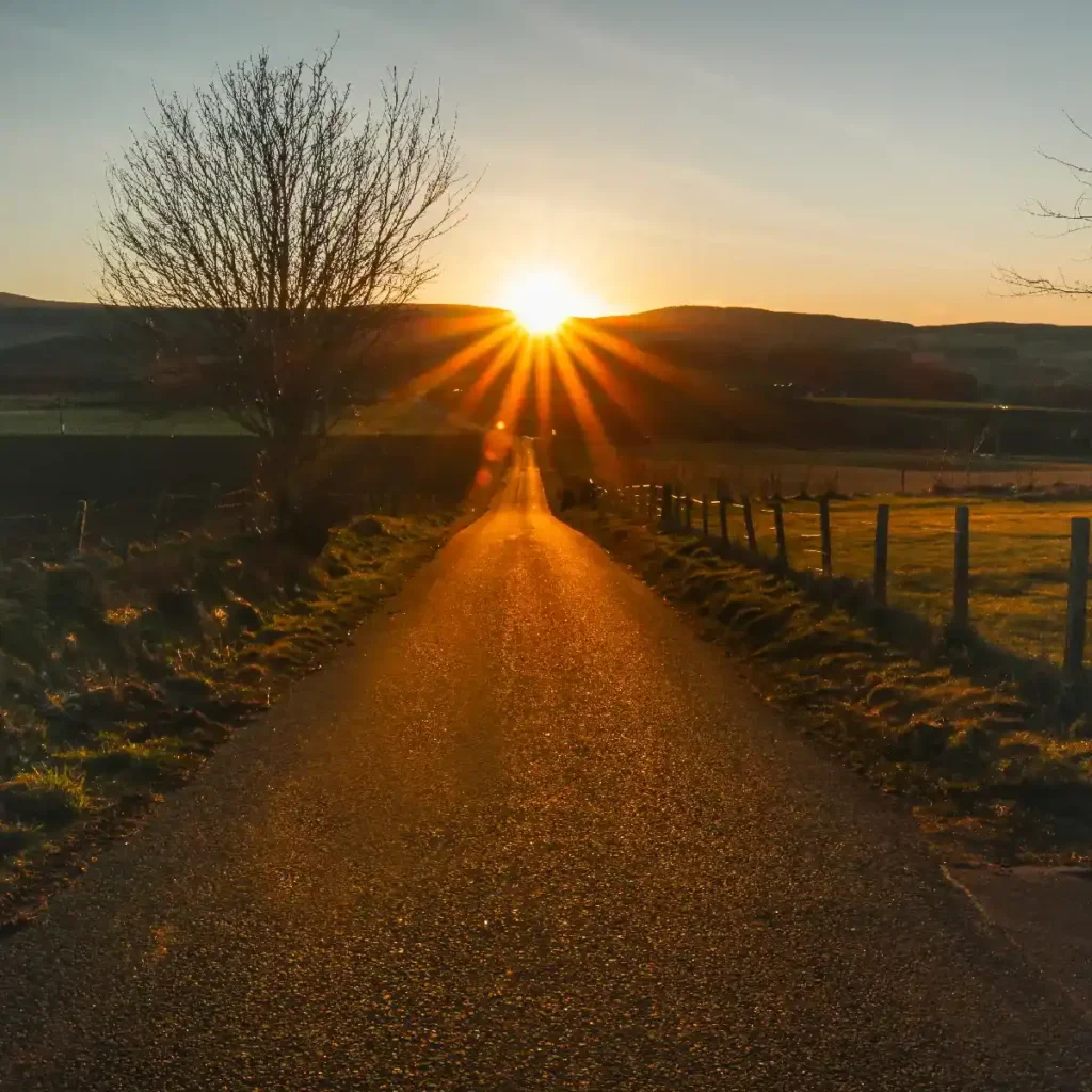 Sun setting in the distance, a long straight road leading directly to the sun. Photo by Torin Liversedge